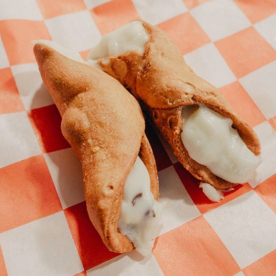 Two golden fried pastries filled with melted white cheese on an orange-and-white checkered paper liner.
