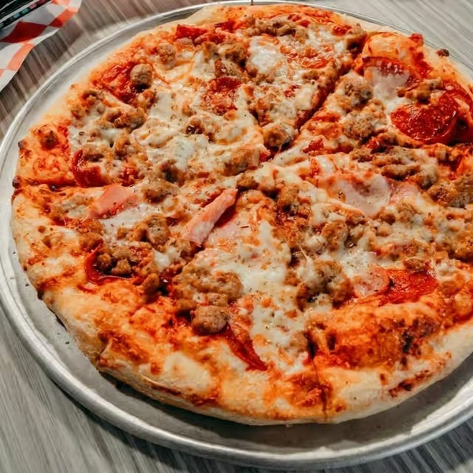 Cheesy pepperoni and sausage pizza served on a metal tray atop a wooden table.